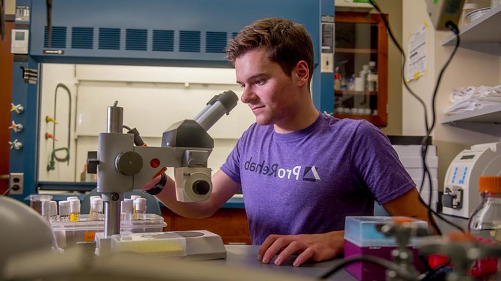 生物学学生穿着ProRehab t恤拿着显微镜