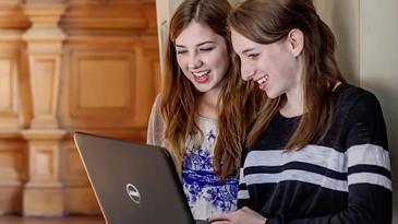 Two female students laughing with laptop